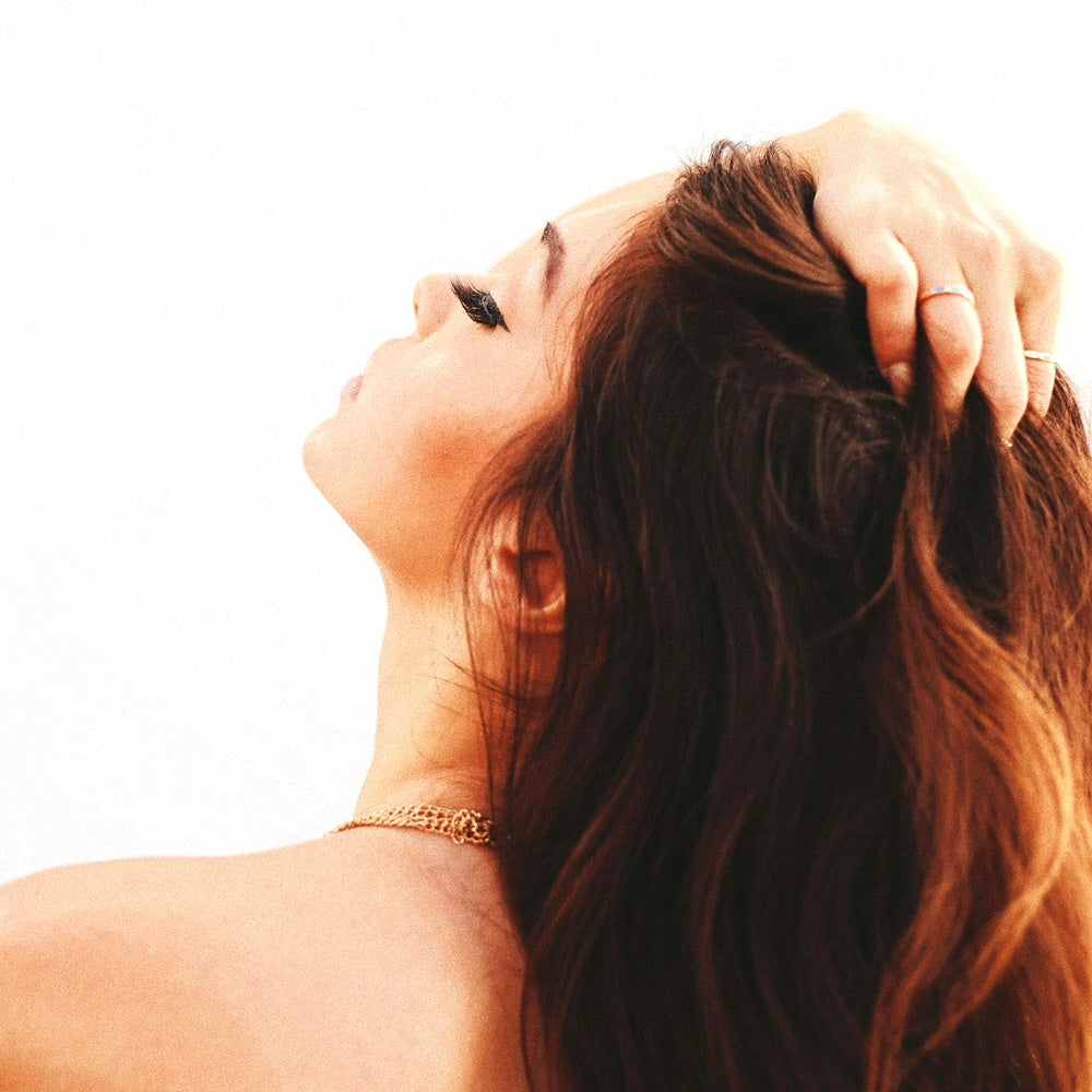 Woman gently massaging her scalp with one hand, showing long red hair against a bright minimal background.