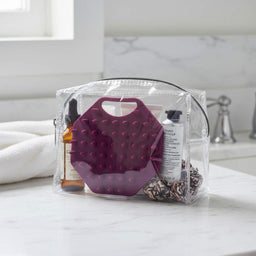 ScrubMeScalp Passionate Purple scalp scrubber inside a clear toiletry bag with haircare products on a marble bathroom counter