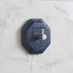 ScrubMe HookMe Breathtaking Blue adhesive hook mounted on a white marble bathroom wall with water droplets on the tiles.