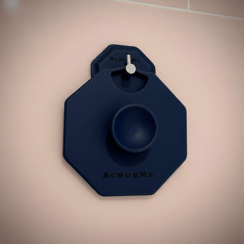 ScrubMeBody Breathtaking Blue silicone body scrubber displayed on a hook against blush pink bathroom tiles, ready to use in the shower.