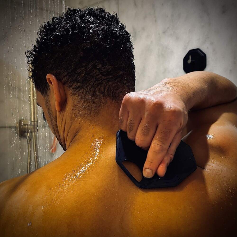 Back view of a man reaching over his shoulder to exfoliate his upper back with the ScrubMeBody Breathtaking Blue silicone body scrubber in the shower.