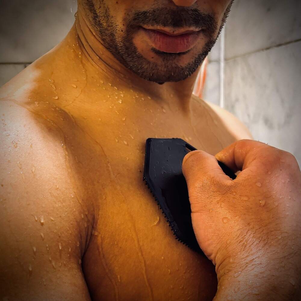 Close-up of a man massaging his upper chest with the ScrubMeBody Breathtaking Blue silicone body scrubber on wet skin in the shower.