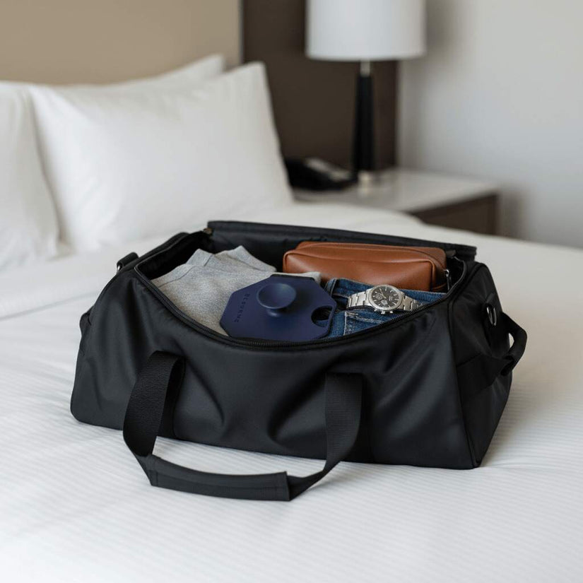 ScrubMeBody Breathtaking Blue body scrubber neatly packed inside a black weekend bag on a hotel bed alongside clothes, wallet and watch.