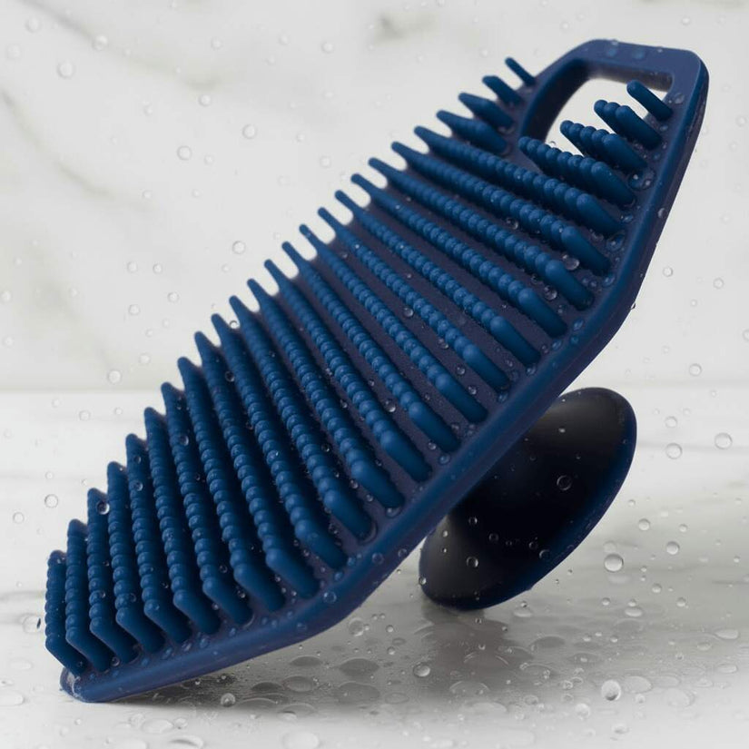 Angled hero shot of Breathtaking Blue ScrubMeFace silicone face scrubber with water droplets on bristles.