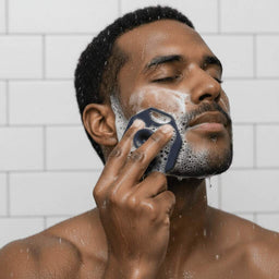 Man washing his face in the shower with the ScrubMeFace Breathtaking Blue silicone cleansing face scrubber.