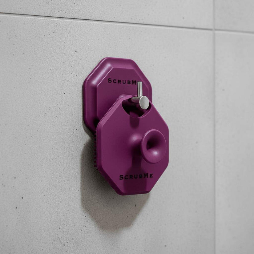ScrubMeFace Passionate Purple face scrubber hanging on matching hook attached to grey bathroom tiles.