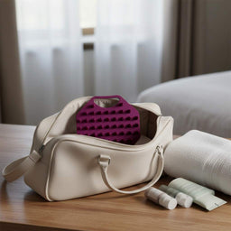 ScrubMeScalp Passionate Purple scalp scrubber packed in a cream travel wash bag on a wooden table next to a white towel and mini toiletries