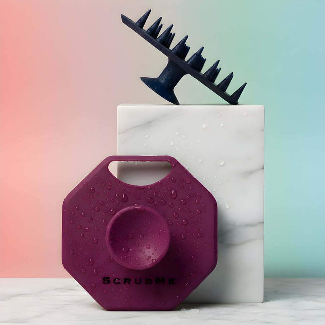Hero image showing ScrubMeScalp scalp scrubbers in Breathtaking Blue and Passionate Purple with water droplets on a marble block and soft gradient background